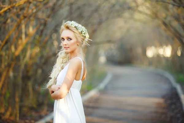 Hermosa mujer rubia en vestido blanco y corona floral en su cabeza. linda persona en callejón . — Foto de Stock
