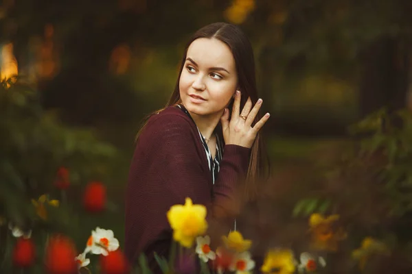 Hermosa chica se sienta en las flores plantadas . — Foto de Stock