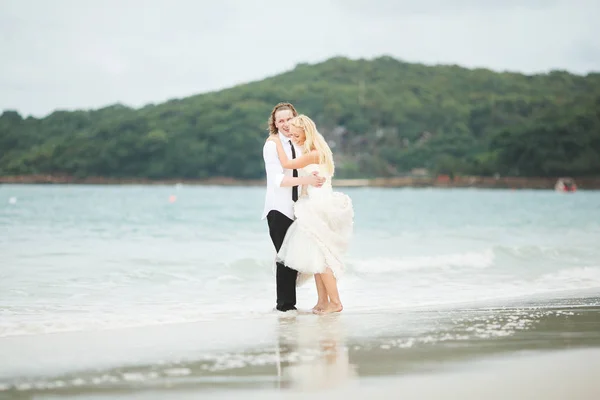 Νύφη και ο γαμπρός που αγκαλιάζει τη θάλασσα. ζευγάρι στην αγάπη στην ερημική παραλία. — Φωτογραφία Αρχείου