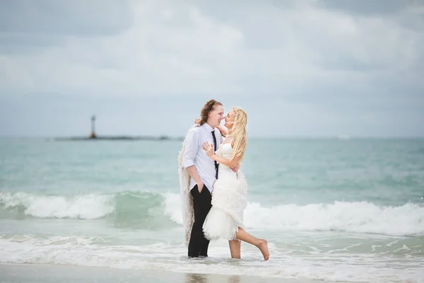 웨딩 드레스에는 바다에서 포옹 하는 신랑의 신부 버려진된 해변에 사랑 하는 커플. — 스톡 사진
