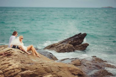 Yeni evli çift kayalık sahilde oturup denize bakmak.