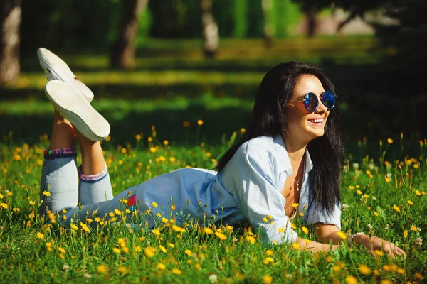 Retrato de mujer hermosa en gafas de sol acostado en la hierba verde de verano con colores brillantes. Chica alegre lleva ropa brillante . — Foto de Stock