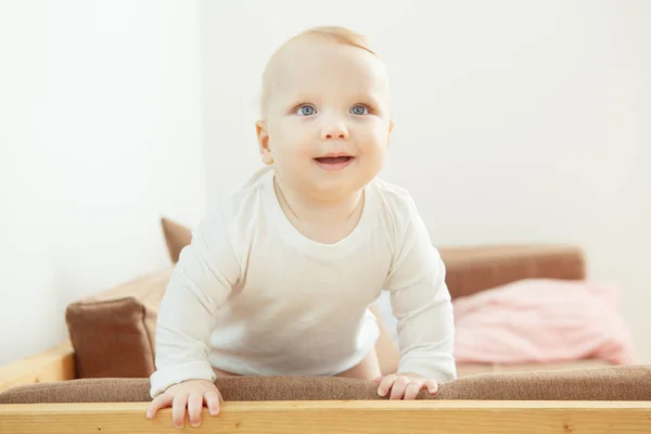 Bebê sorrindo de pé no sofá contando com suporte . — Fotografia de Stock