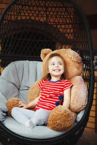 Menina sentada na cadeira no terraço com urso de brinquedo . — Fotografia de Stock