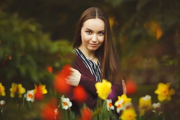 Menina bonita senta-se nas flores plantadas . — Fotografia de Stock