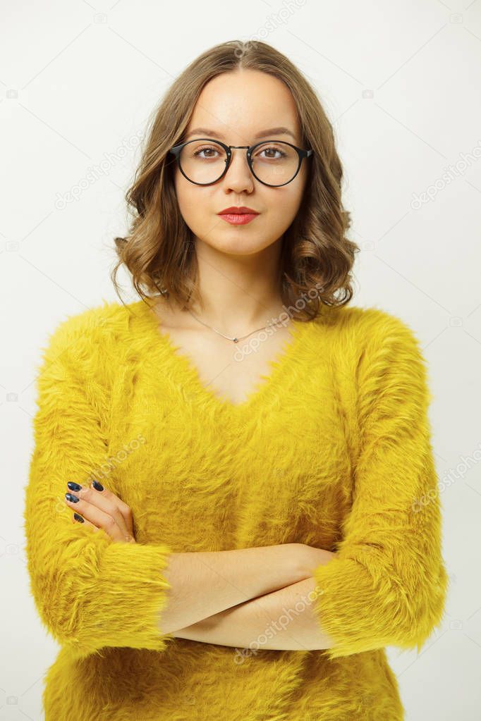 Vertical portrait of serious girl with round spectacles, wears bright clothes, has confident and calm expression, stands over white isolated background.