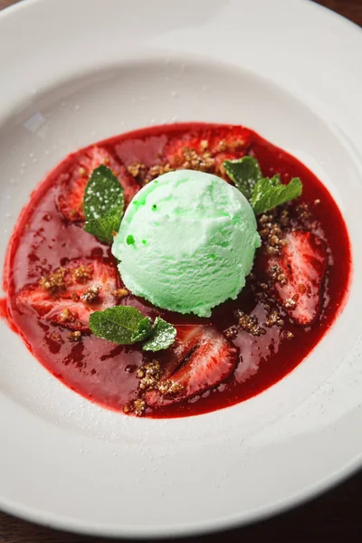 stock image vertical close-up shot of delicious mint ice cream scoop green with red jam and mint leaves on white plate. Top view. summer seasonal menu.