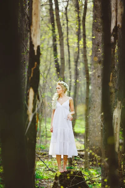 Mujer joven perdida con el pelo rubio en el bosque vestido blanco entre árboles . — Foto de Stock