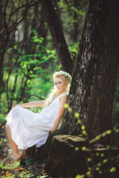 Bela mulher em vestido branco senta-se por árvore floresta verde . — Fotografia de Stock
