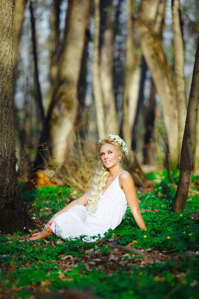 Hermosa mujer en vestido blanco se sienta en la hierba en medio de un bosque de verano . —  Fotos de Stock