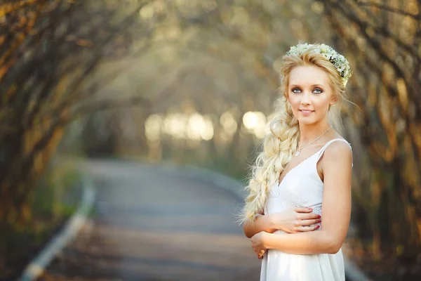 Hermosa mujer rubia en vestido blanco y corona floral en su cabeza. linda persona en callejón . — Foto de Stock