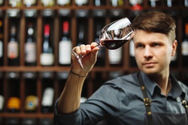 Arka planda bir şişe kırmızı şarap, erkek şarap garsonu içkinin değerini biliyor.