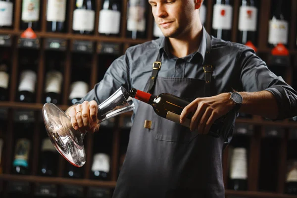Bartender pours red wine in transparent vessel in cellar — Stock Photo, Image