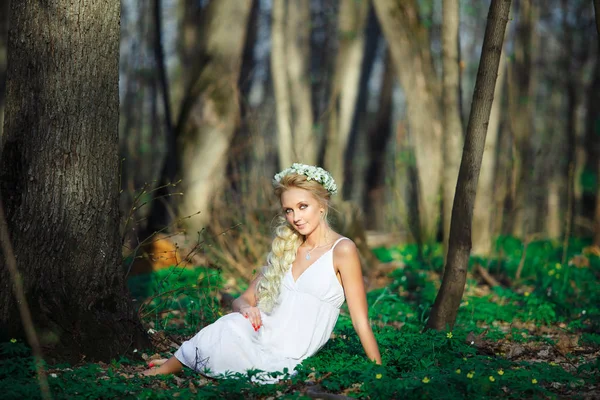 Bela mulher de vestido branco senta-se na grama no meio de uma floresta de verão . — Fotografia de Stock