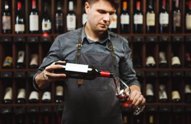 Erkek şarap garsonu kırmızı şarabı uzun saplı şarap bardaklarına dolduruyor..