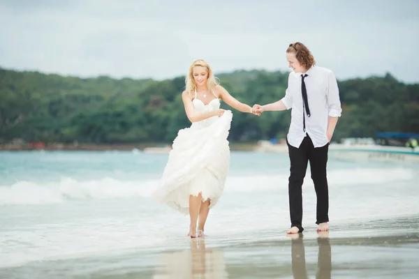 Bruid in trouwjurk en bruidegom lopen op de zee. Bruiloft op een verlaten strand. — Stockfoto