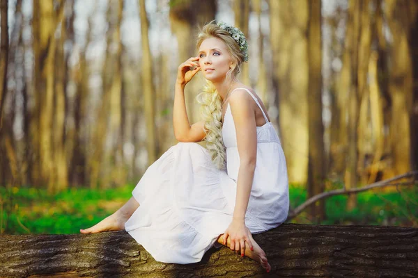 Schöne Frau im weißen Kleid sitzt am Baum grünen Wald. — Stockfoto
