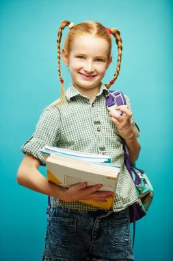 Oturmak sırt omuzlar ve elinde defter ile gülümseyen genç, iyi bir ruh hali var, okul üniforması giyer izole mavi arka plan üzerinde duruyor. Okula kız öğrenci.