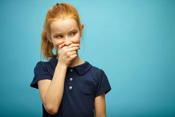 Portret poziomy sly piegowaty dziewczyna z rude włosy obejmuje jej usta i wygląda odległości na niebieskim tle na białym tle. — Zdjęcie stockowe