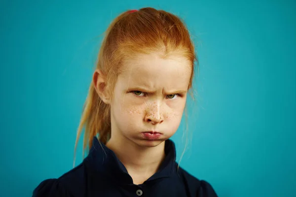 Fille aux cheveux roux avec un visage offensé et la bouche gonflée regarde dans la caméra, sillonné ses sourcils, a une expression négative, démontre le mécontentement ou l'insatisfaction, portrait sur bleu isolé . — Photo