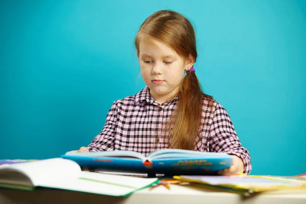 Retrato aislado del escolar en el escritorio sosteniendo un libro en sus manos y leyendo con entusiasmo. Chica joven en primer grado . — Foto de Stock