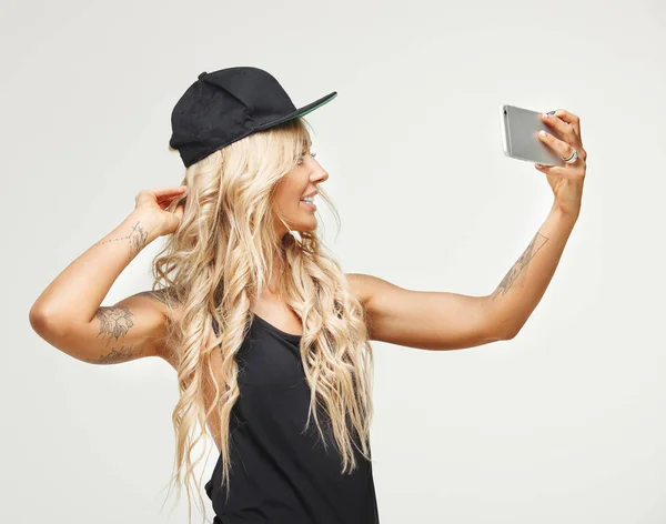 Retrato de la cintura de la mujer rubia de perfil hace selfie en el teléfono un fondo aislado. chica tatuada tomando fotos a sí misma con el teléfono inteligente . —  Fotos de Stock
