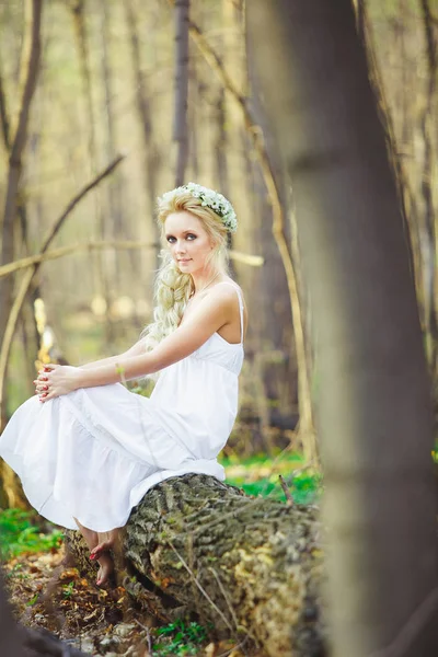 Mooie vrouw in witte jurk zit door groene boom bos. — Stockfoto