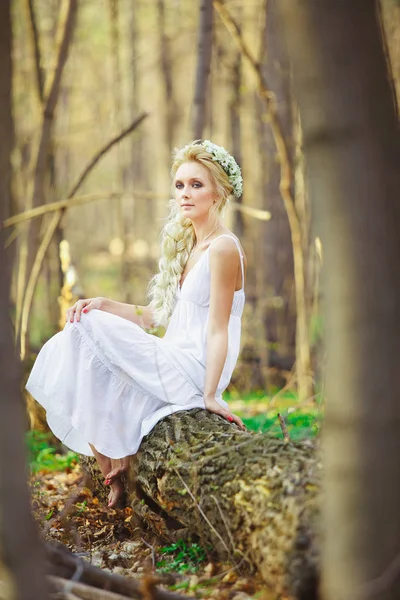 Beautiful woman in white dress sits by tree green forest. — Stock Photo, Image