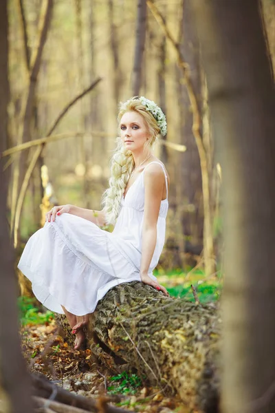 Bela mulher em vestido branco senta-se por árvore floresta verde . — Fotografia de Stock