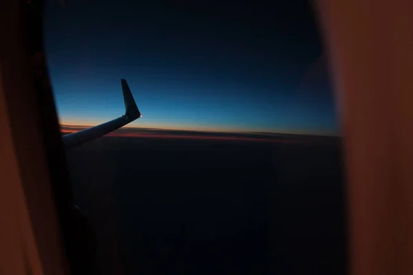 Ala del plano desde el ojo de buey de la ventana en el cielo crepuscular . —  Fotos de Stock