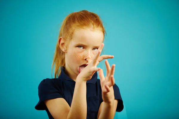 Engraçado menina brinca com você, furar a língua para fora e mostra dedos gestos impertinentes no fundo isolado azul . — Fotografia de Stock