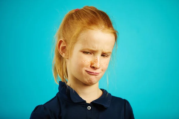 Retrato de criança frustrada com olhar apertado olhando para longe, expressando nojo, close-up de menina ruiva no fundo isolado azul . — Fotografia de Stock
