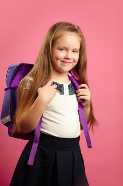 Güzel kız onun omuzlarında sırt çantası ile izole pembe mutlu duruyor, iyi bir ruh hali var, heyecanla okula gidiyor. Neşeli çocuk öğrenmek üniforma hazır.