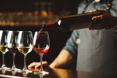 Barman nalévá červené víno ve sklenicích na dřevěnou barovou linku