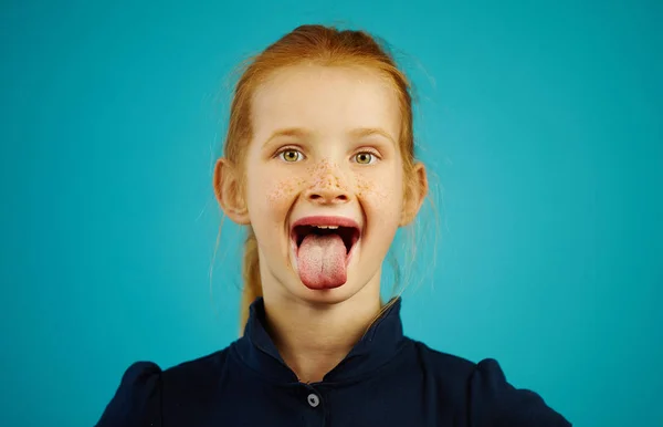 Chica alegre con pecas y el pelo rojo abrió su boca ancha, lengua sobresaliente, sobre un fondo azul aislado. Chico travieso tonteando . — Foto de Stock