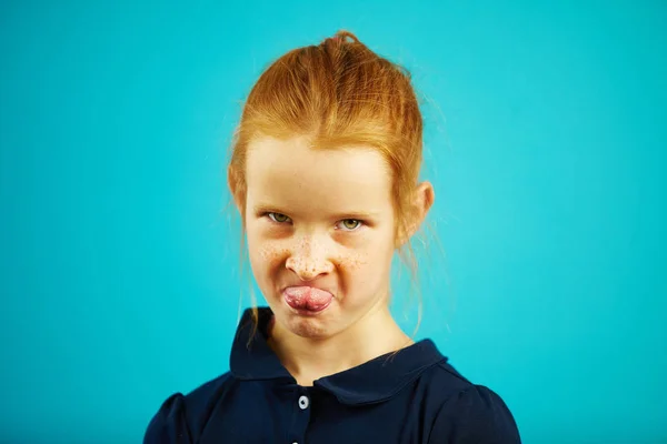 青色の背景の肖像画間近の気まぐれな表情で怒っている女の子舌を示しています、赤い髪とそばかすが、機嫌が悪い難しい文字を示します、. — ストック写真