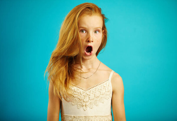 Red haired girl in white dress with surprised expression opens her mouth and eyes wide, shows a strong emotion of fear or shock, is shocked and stunned.