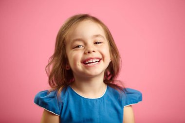 Neşeli küçük kız çekici gülümseme ve pembe izole arka planda, içten kahkaha ile sevinç içten duygular ifade eder, keyfi yerinde.