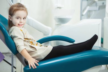 Küçük çocuk konforlu deri dişçi koltuğuna oturur