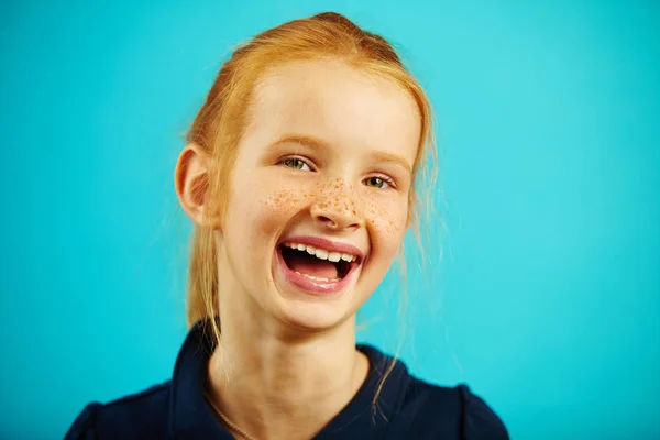 Retrato close-up de menina rindo alegre com cabelo vermelho e sardas em fundo isolado azul. Criança feliz expressa uma emoção sincera de felicidade . — Fotografia de Stock
