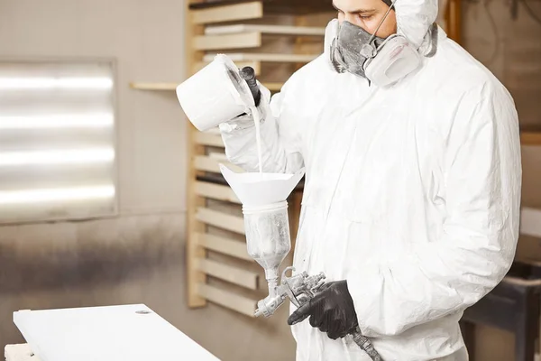 El hombre vierte pintura en el pulverizador antes de pintar la madera . — Foto de Stock