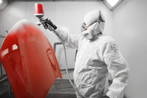 Trabalhador pintor de spray em luva protetora com pulverizador de aerógrafo pintando elemento do corpo do carro vermelho na câmara de pintura branca . — Fotografia de Stock