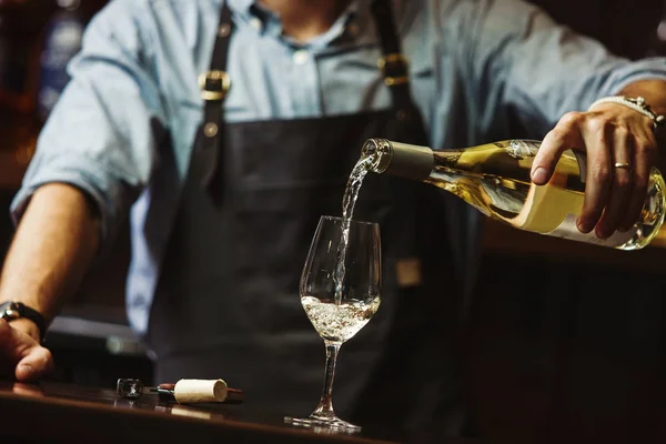 Чоловічий сомельє наливає біле вино в довгоногі келихи . — стокове фото