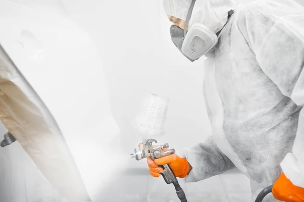 Spraymålare arbetare i skyddshandske med airbrush pulveriserare målning bil kropp i vit färg kammare. — Stockfoto