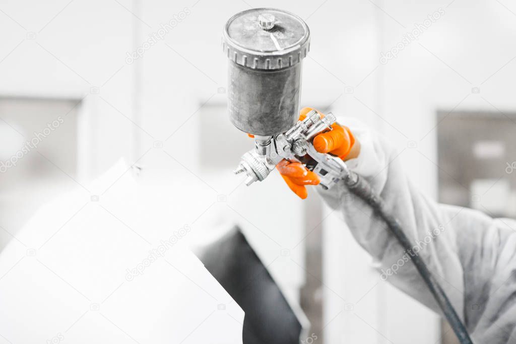 Male repairman painter in chamber painting automobile car elements. Worker paints the vehicle in white with a spray gun.