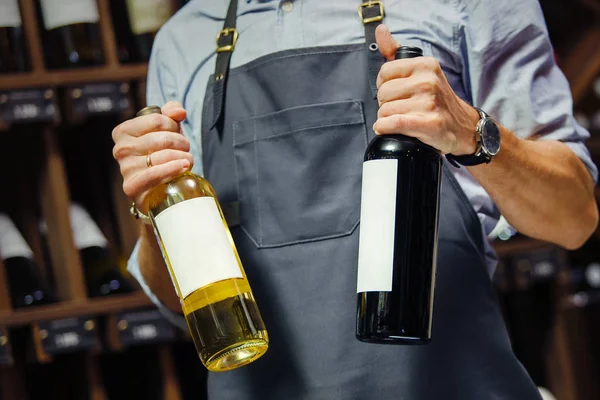 Young sommelier holding bottle of red wine in cellar