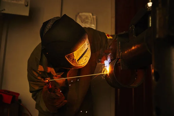 Worker in safety mask welds metal at industrial enterprises.