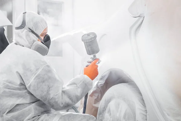 Художник с пневматическим пистолетом распыляет белую краску на автомобиль в машинном отделении техобслуживания. — стоковое фото