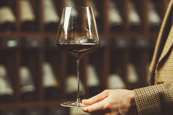 Copo de vinho tinto na mão sommelier na adega com fundos de garrafas . — Fotografia de Stock