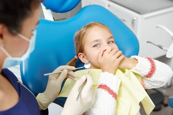 Menina parece assustada, cobrindo a boca do dentista com ferramentas médicas . — Fotografia de Stock